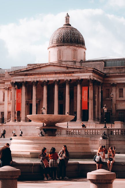 Nighttime view of a historic neoclassical building with a prominent central dome illuminated with warm lighting. The structure features tall, rounded columns supporting a triangular pediment, with a s